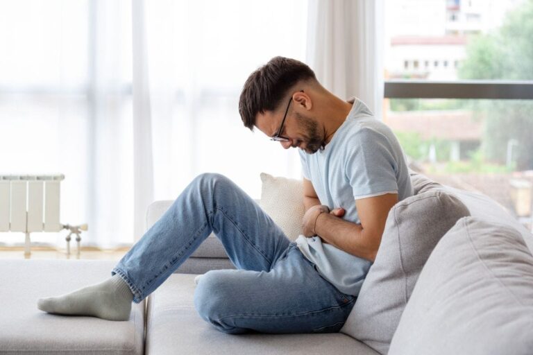 Man sitting on couch holding his stomach.