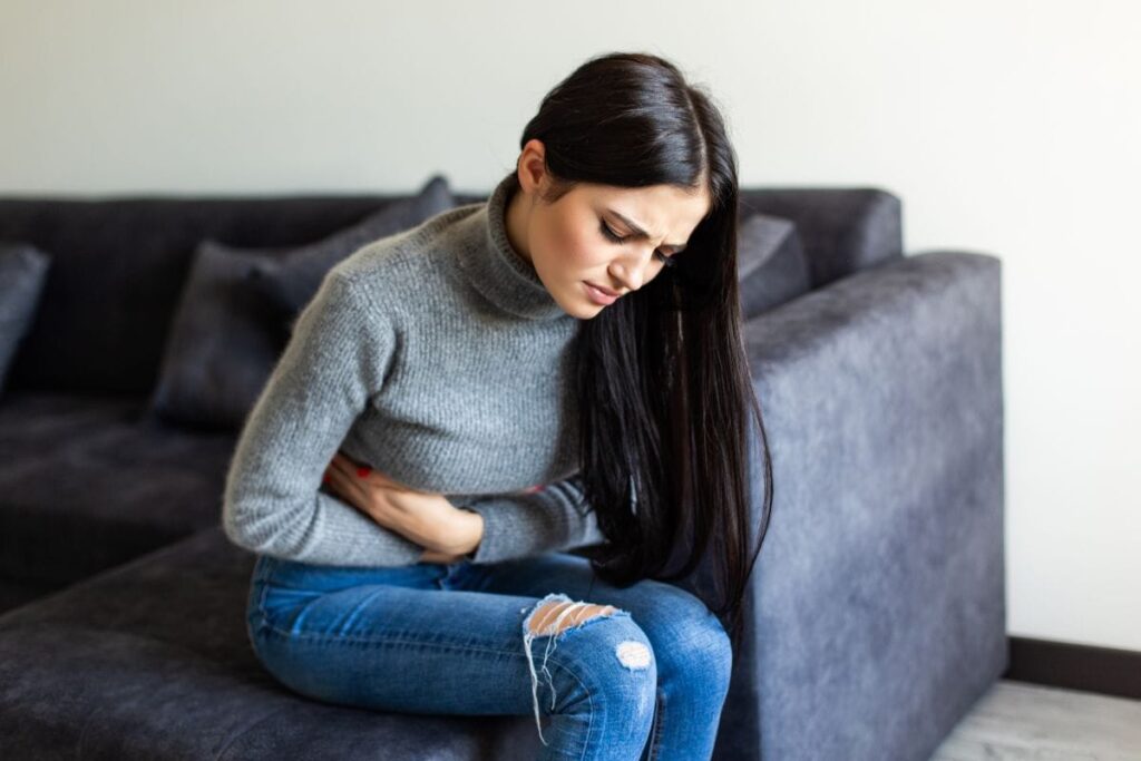 woman sitting on couch holding his stomach.