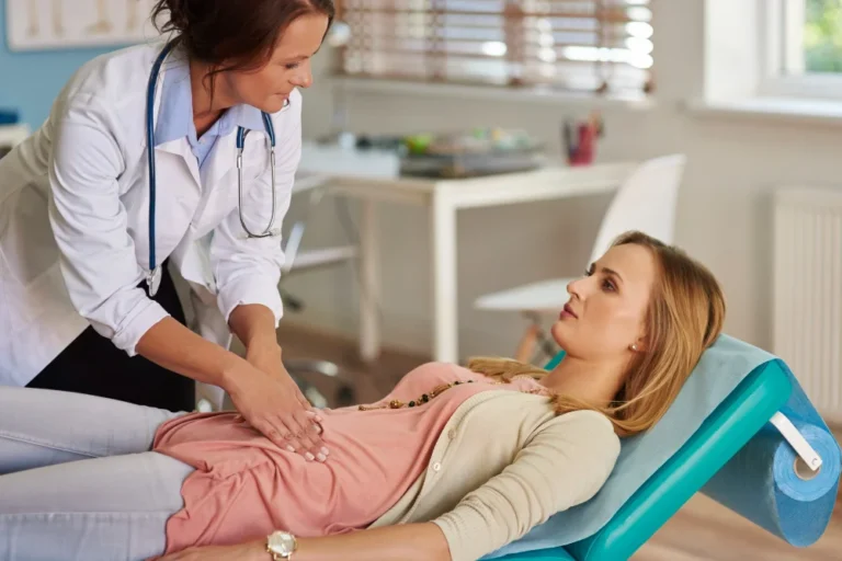Doctor examining patient's abdomen on medical chair.