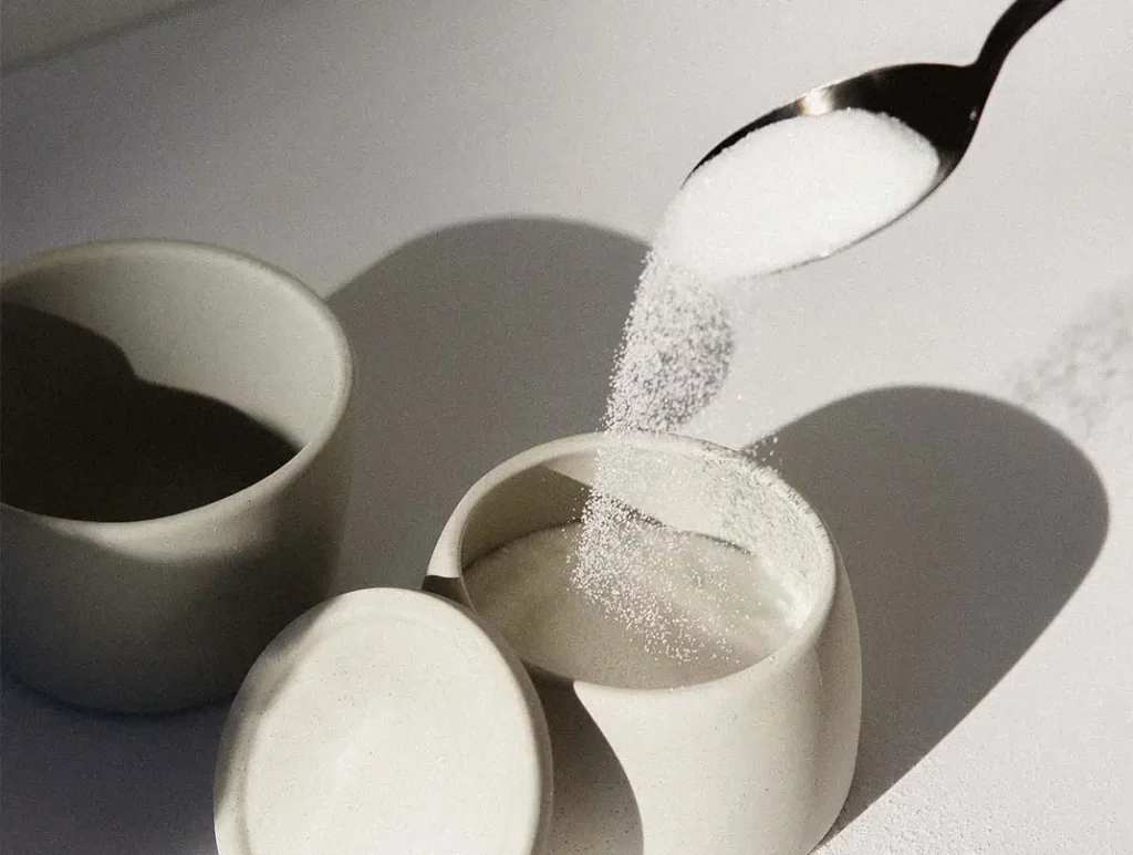 Spoon pouring sugar into a container.